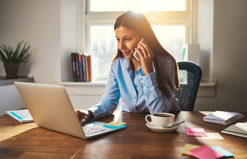 A person on her cell phone looking at the computer